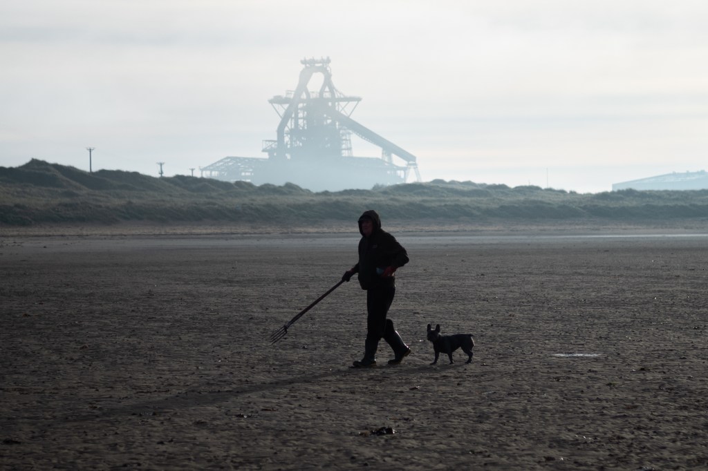 Person on beach with steeelworks in background