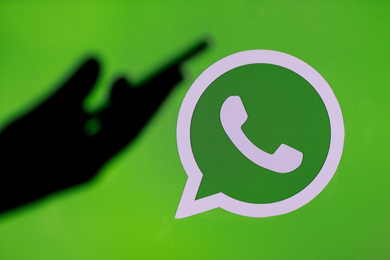 Silhouette of a hand holding a phone, in front of the WhatsApp logo
