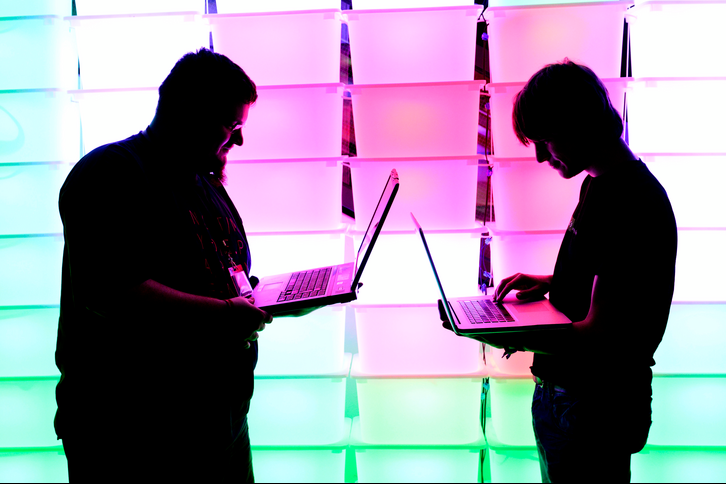 Participant hold their laptops in front of an illuminated wall illustrating insider dealing