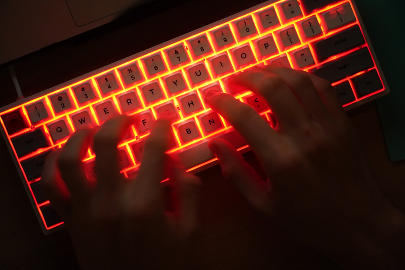 A young man types on an illuminated computer keyboard typically favored by computer coders
