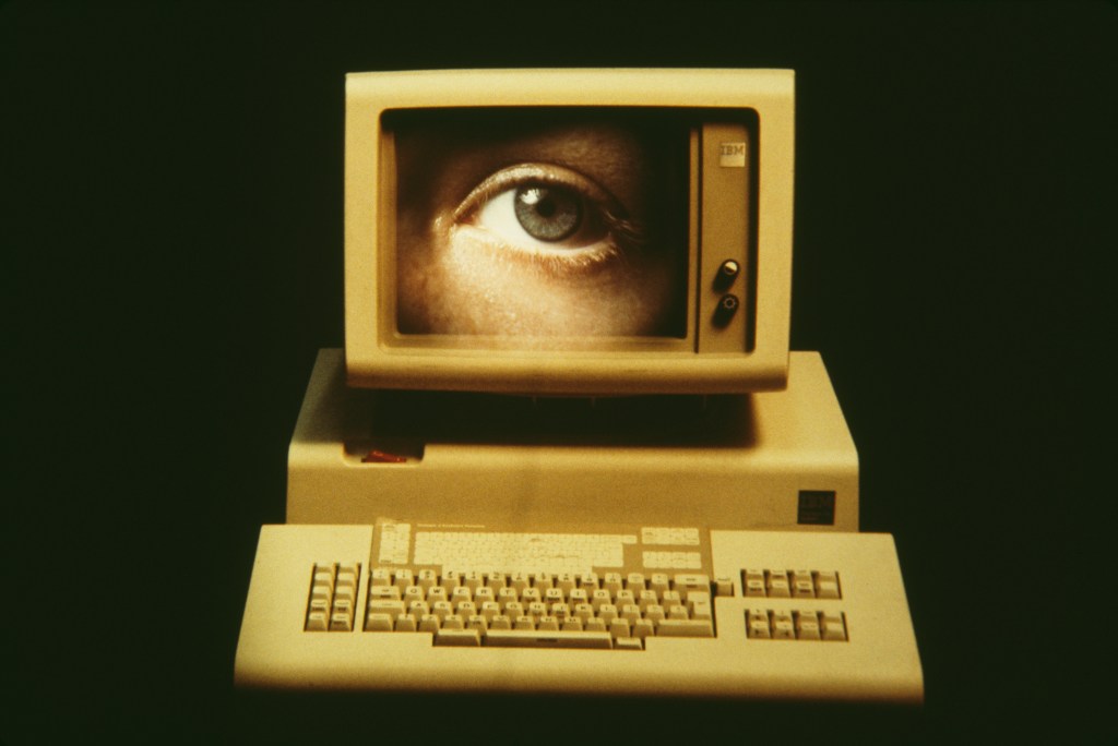 Image of an old computer monitor and keyboard with an ever-watchful eye appearing in the monitor.