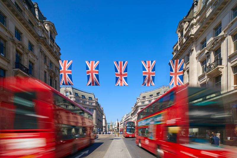 Union Jack flags across Regent Street with London red busses blurred.
