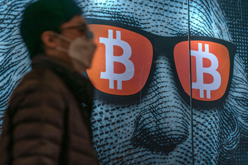 Pedestrians walk past a display of cryptocurrency bitcoin.