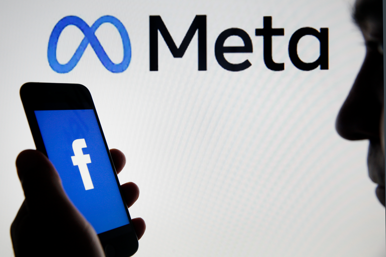 the Facebook logo is displayed on the screen of an iPhone in front of a Meta logo