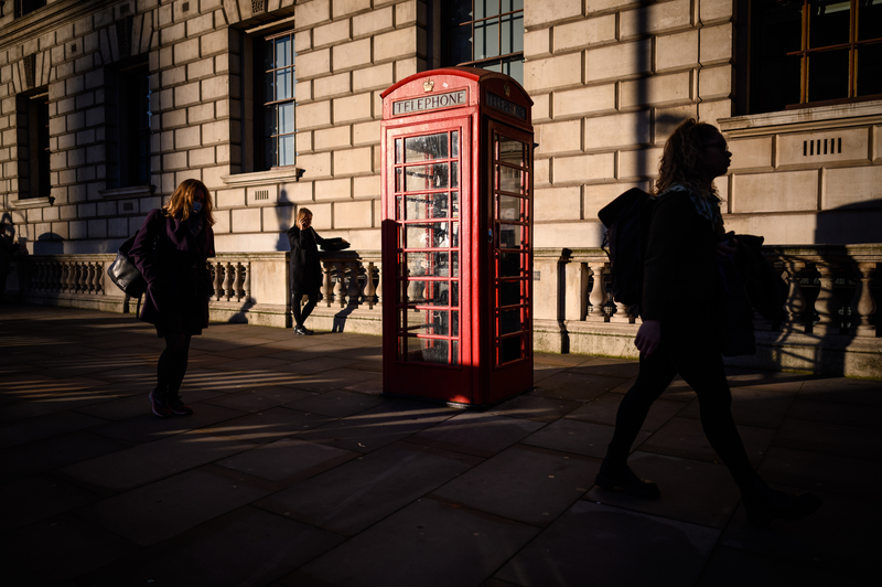 A woman stops to use her mobile phone next to a traditional red telephone box in London, England