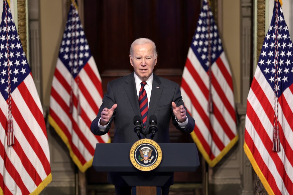Image of President Joe Biden speaking a a podium flanked by American flags.