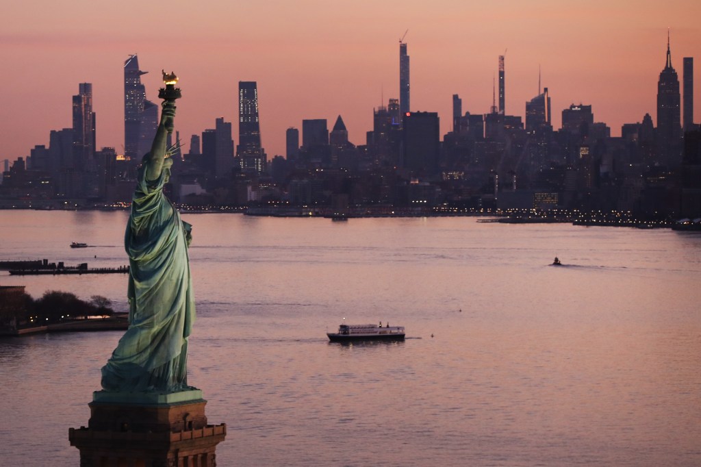 Image of the Statue of Liberty and NYC skyscape at sunset.
