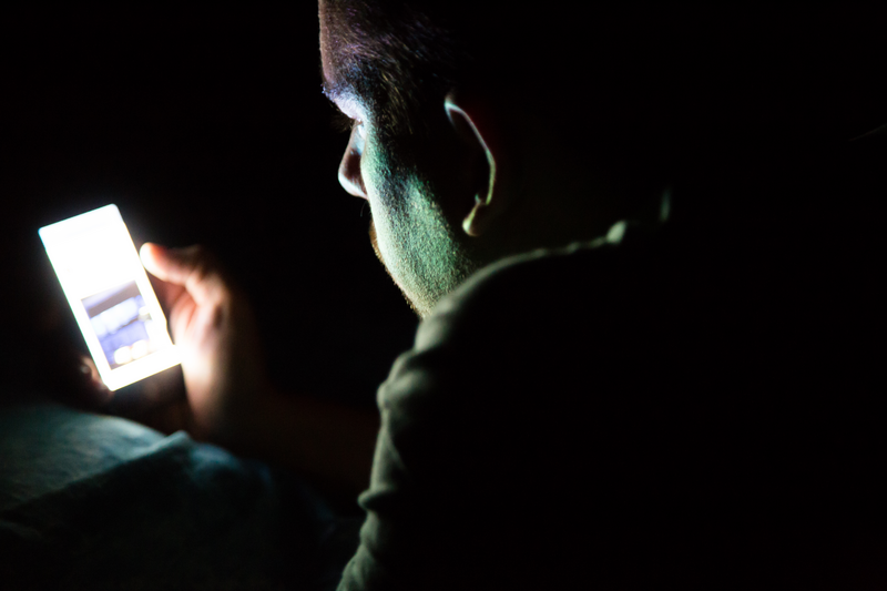 Man laying on bed at late night in a dark room checking his smartphone.