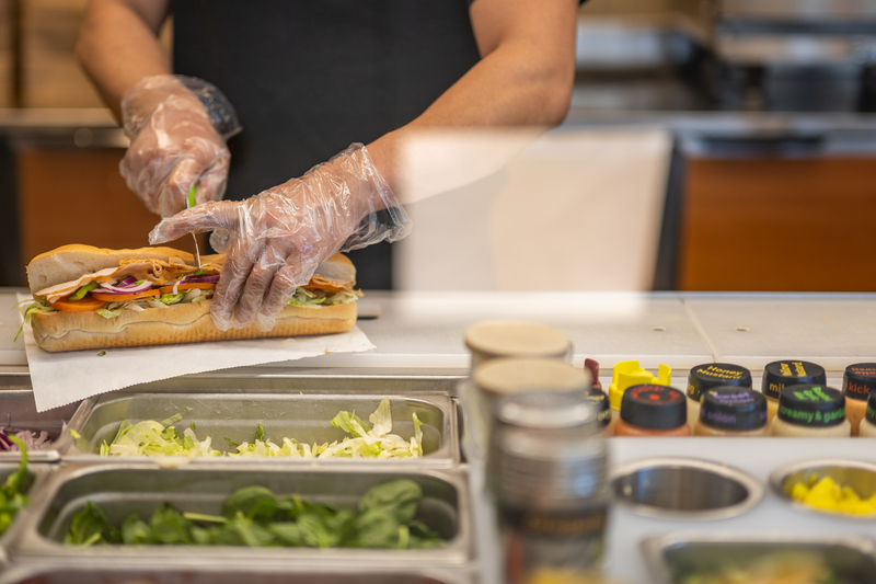 An employee halves a Subway sandwich at a Subway restaurant.