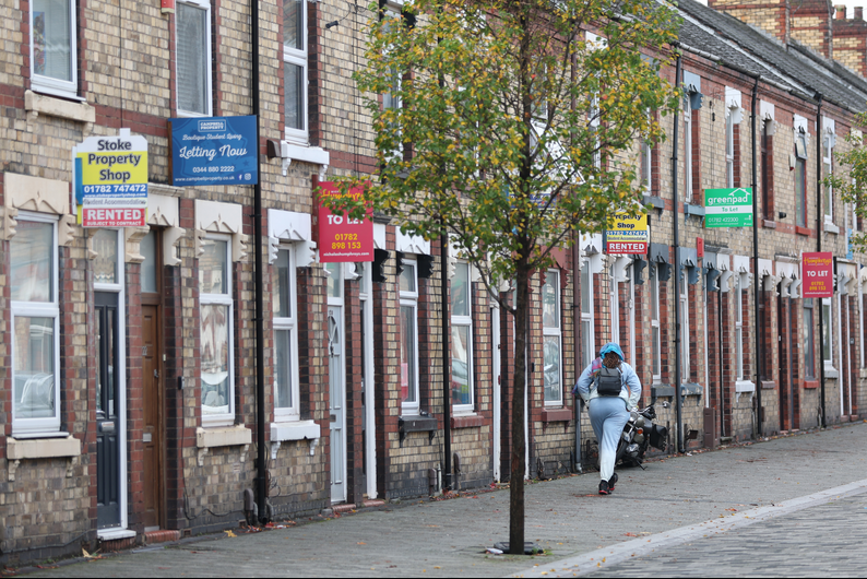 Cost of living crisis - A lady walks past a street of terraced houses advertising properties are rented or to let.