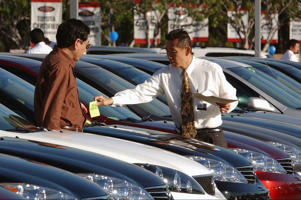 Image of a customer checking out a car in a car dealership parking lot.