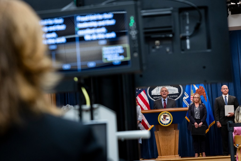 Image of US Attorney General Merrick Garland near a large data screen.