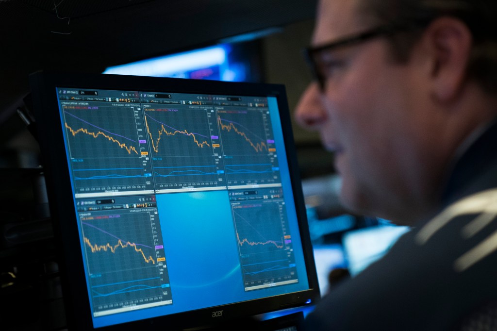 Image of a man in front of a computer showing stock-trading data.