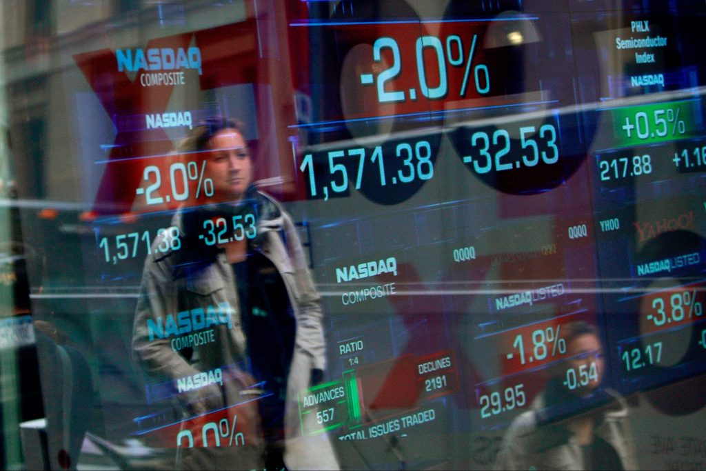 Image of a woman walking past the Nasdaq Market site tickers in Times Square, New York City.