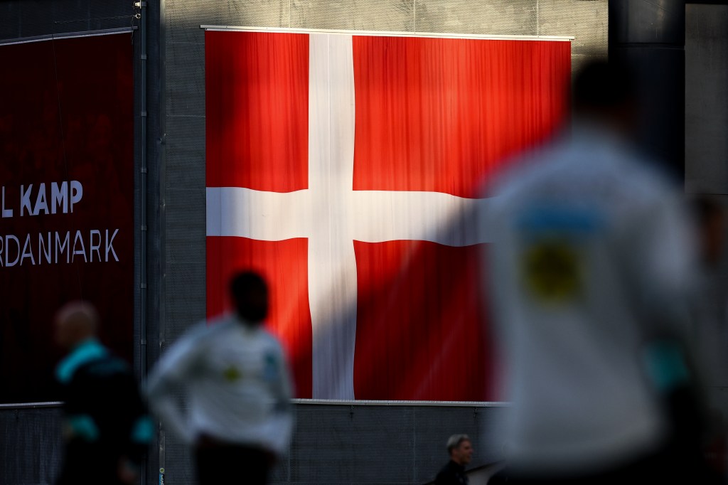 The Danish flag is seen on a wall, with blurry people in front of it.