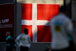 The Danish flag is seen on a wall, with blurry people in front of it.