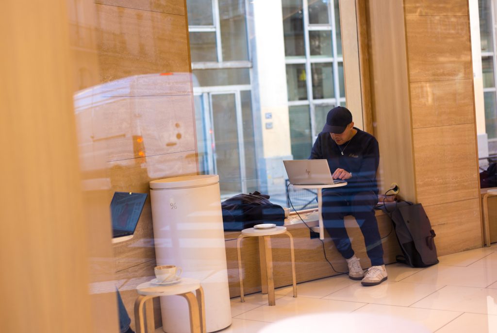 A man works on a laptop near a window in a cafe.