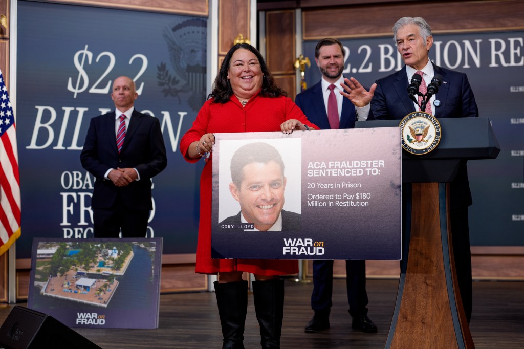 A photo of a press conference by the Centers for Medicare & Medicaid Services and Vice President JD Vance, showing 3 men, including the vice president and CMS Administrator Mehmet in suits, and a woman in a red dress holding up a poster with information about ACA-related fraud.