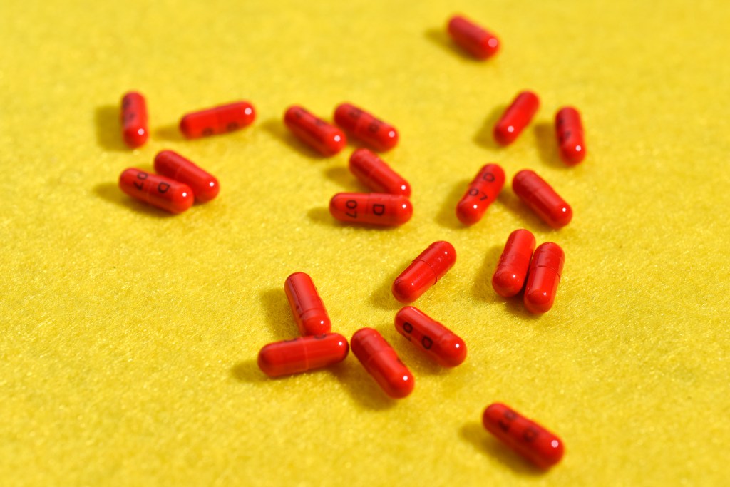 A photo of red medication capsules scattered on a yellow surface.