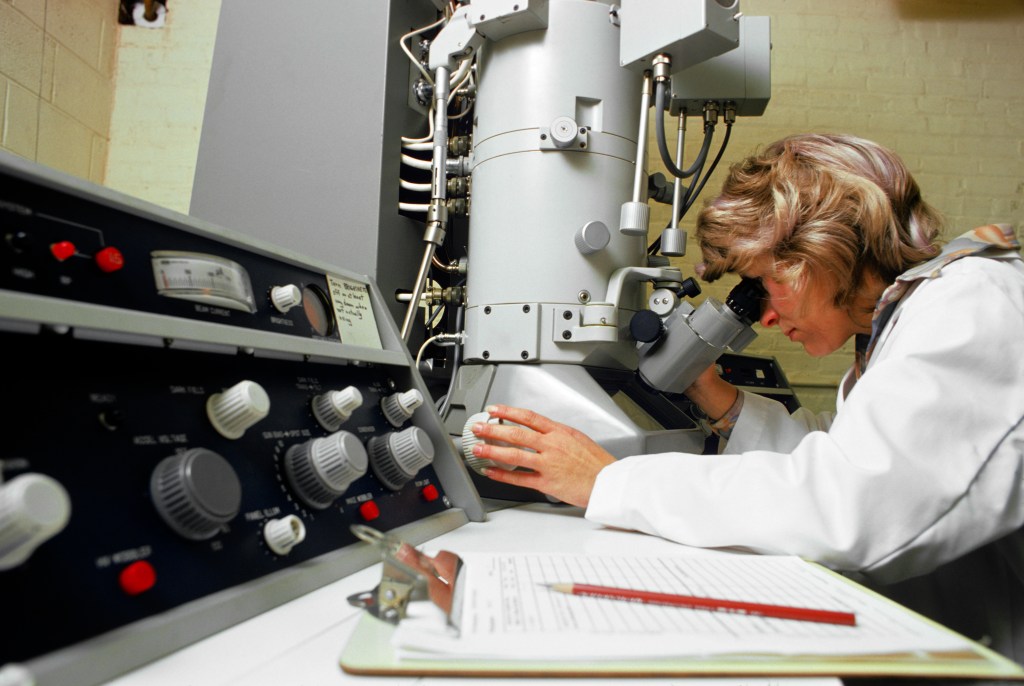 A woman looking in a microscope wearing a white lab coat in a lab.