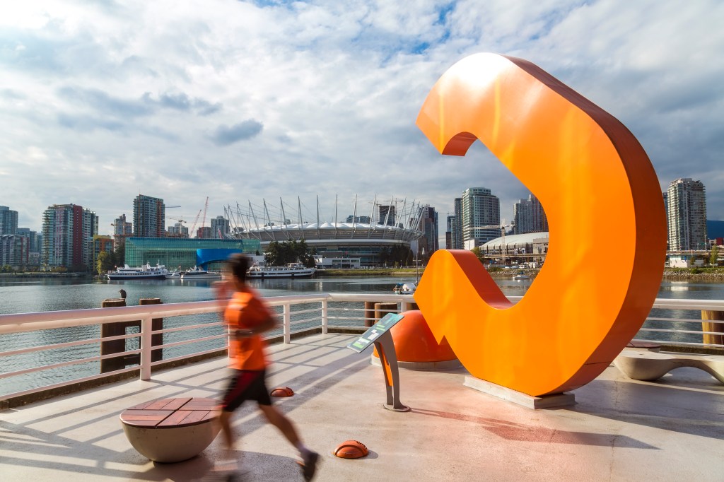 Orange question mark art installation along False Creek waterfront with BC Place Stadium in background in, Downtown Vancouver, British Columbia, B.C. Canada.
