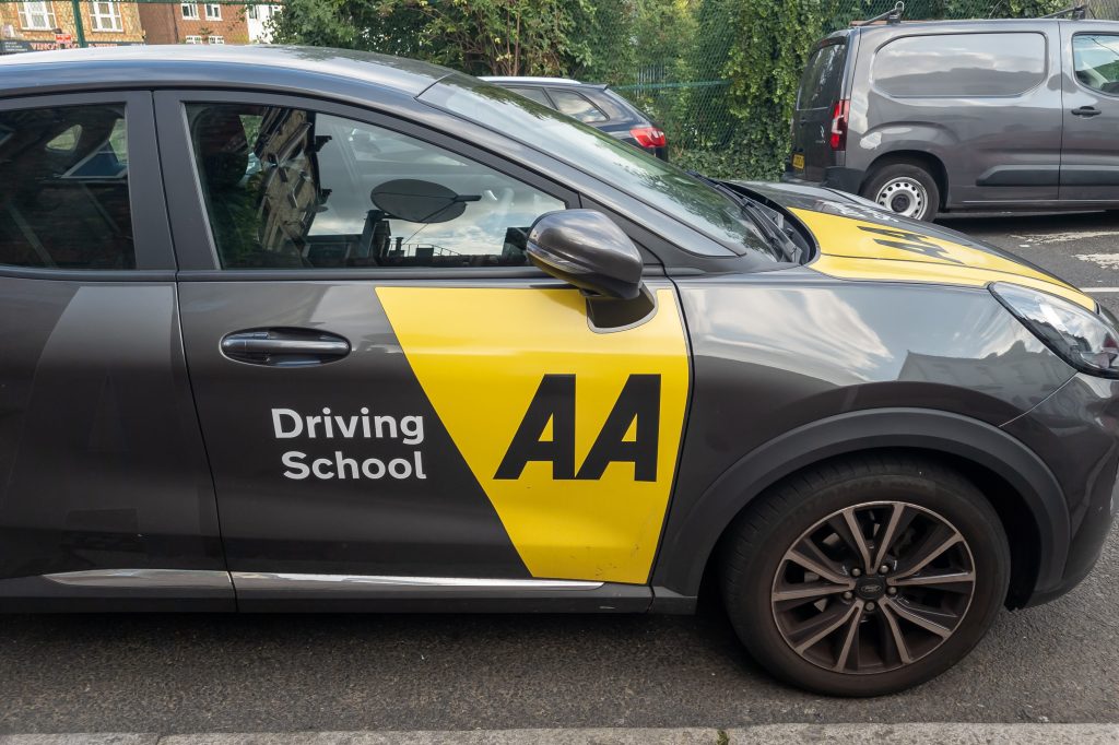 Side view of an AA Driving School vehicle parked on a street.