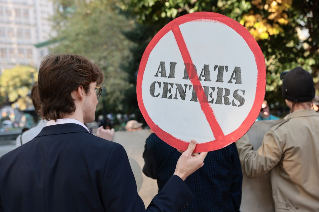 A man holds a sign with a line running through it saying "AI Data Centers."