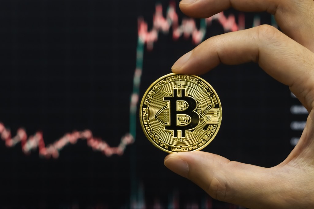 Image of a bitcoin with a chart in the back showing its price movement.