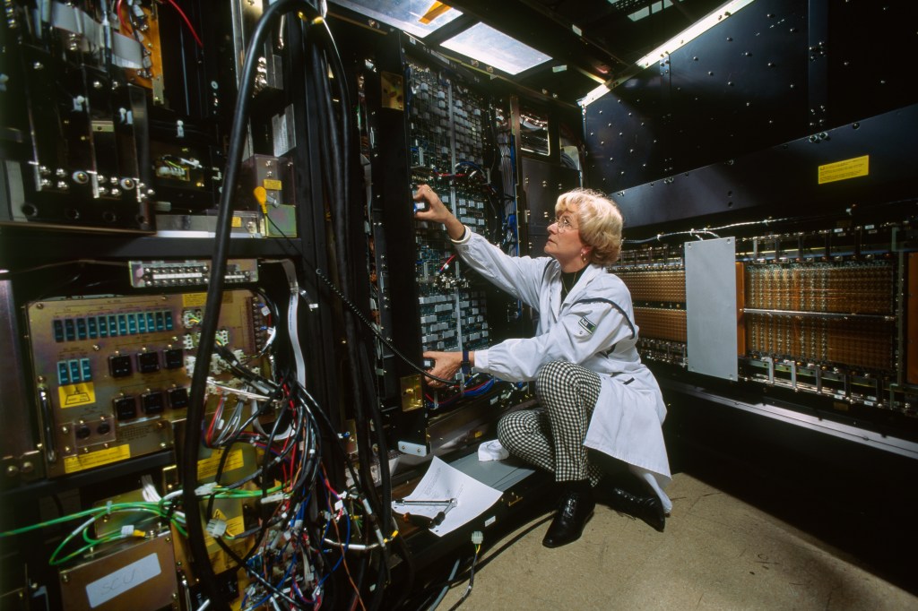 A female information systems operator in a light blue worker coat tests the performance of computer parts