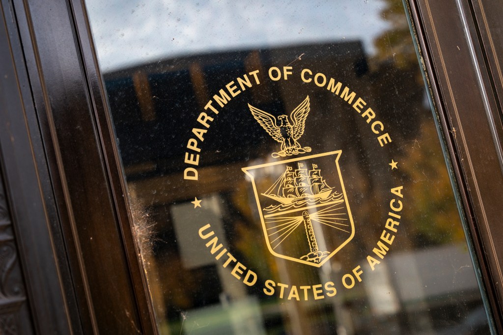 A photo of the seal of the US Department of Commerce in gold lettering on a glass window.