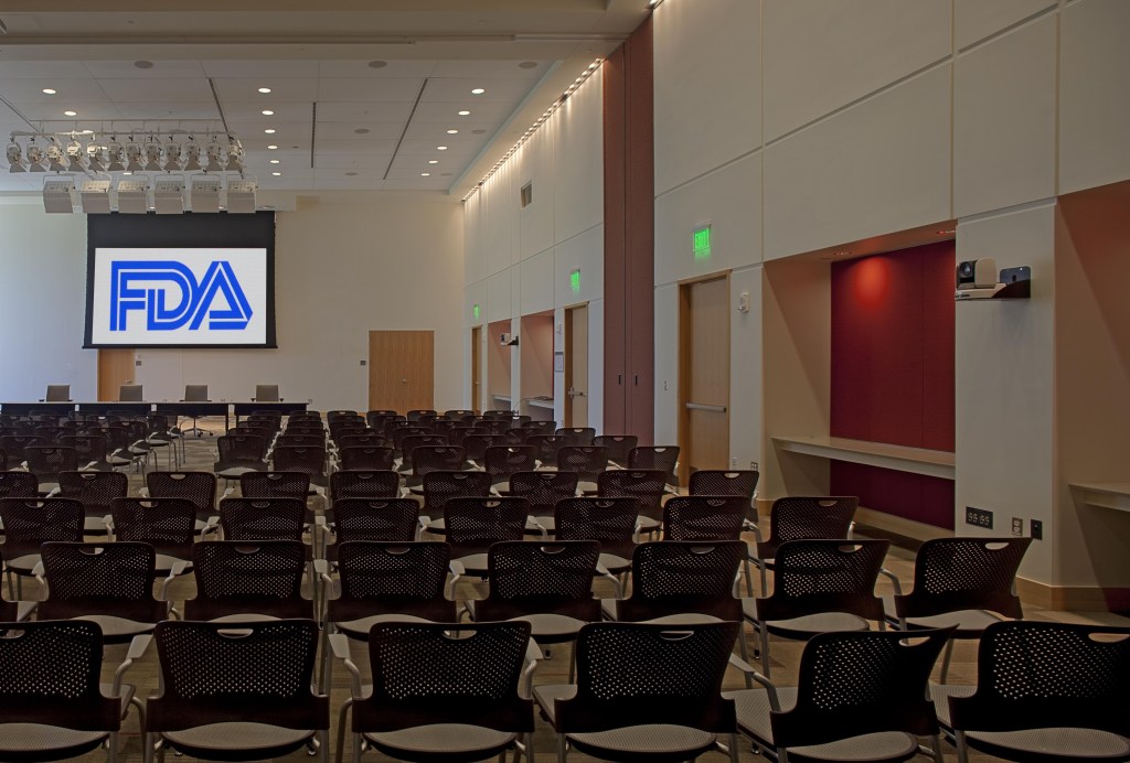 Rows of chairs face the stage and FDA logo screen in the Great Room of Building 31 at the U.S. Food and Drug Administration
