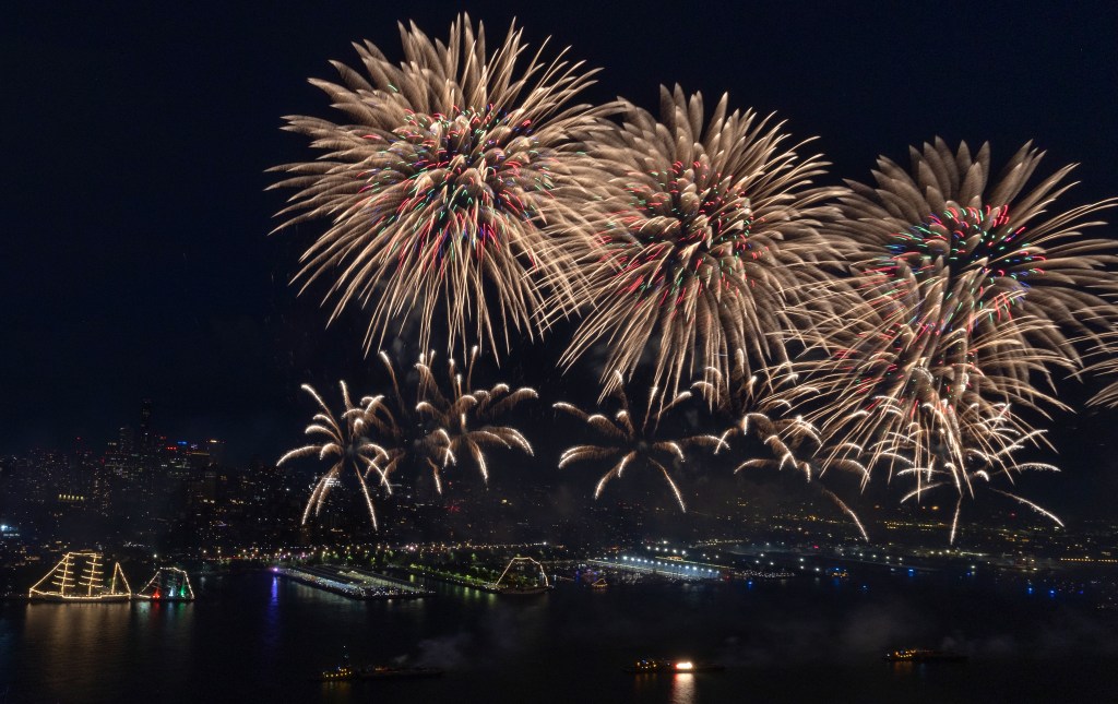 A photo of several large firework stars expoding over the East River in New York City