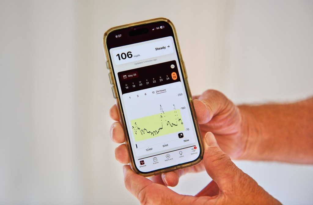 A photo of two white hands holding a cellphone with a blood-sugar reading on a screen.