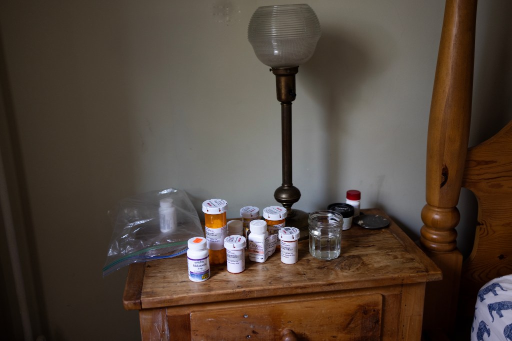 Several medication bottles on a wooden bedside table and small metal lamp.