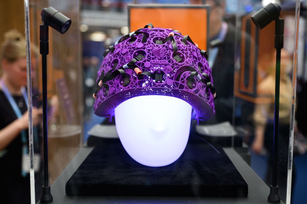 A photo of a purple dome or headpiece of computer part and wires on a fake model head illuminated from within at a medical device expo.