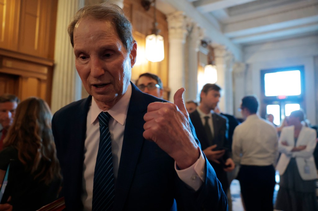 A photo of Democratic Senator Ron Wyden of Oregon pointing his thumb behind him in a crowded hallway in the capital building,