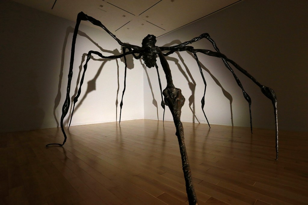 A photo of artist Louise Bourgeois's spider sculpture surrounded in shadows in an art gallery.