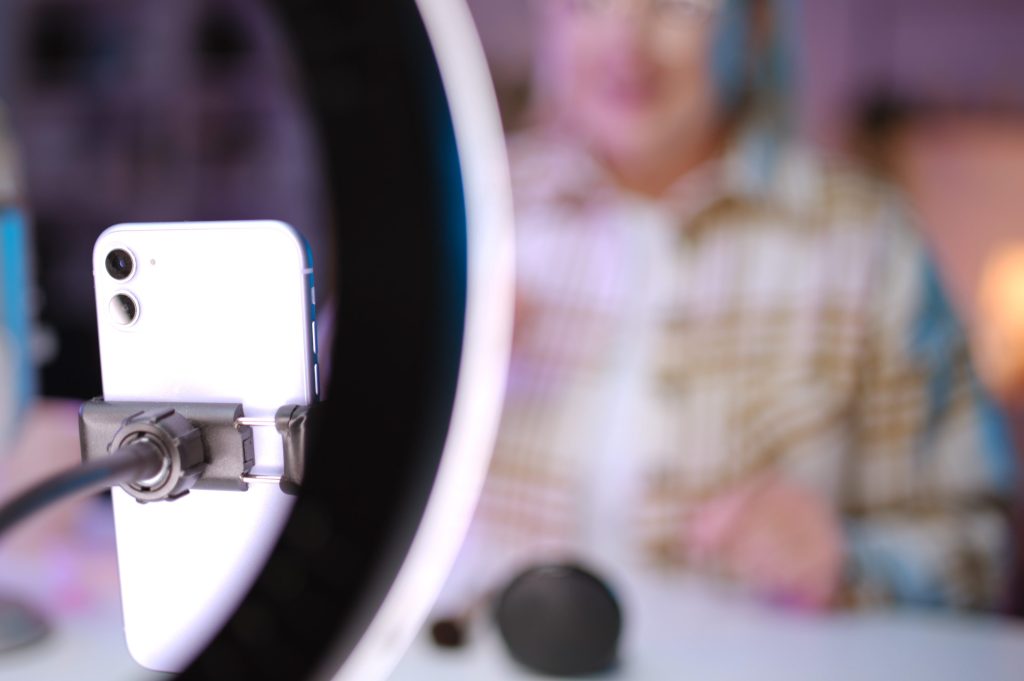 A person is recording a video for a blog using a smartphone and a ring light.
