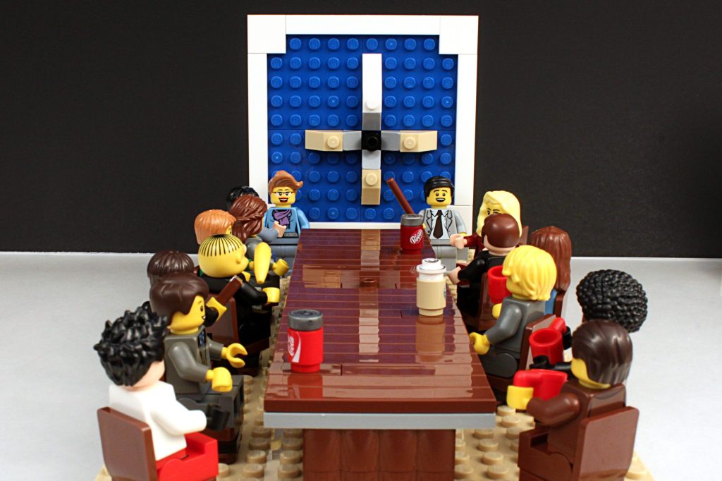 Studio shot of Lego minifigures portraying board meeting scene on white background.