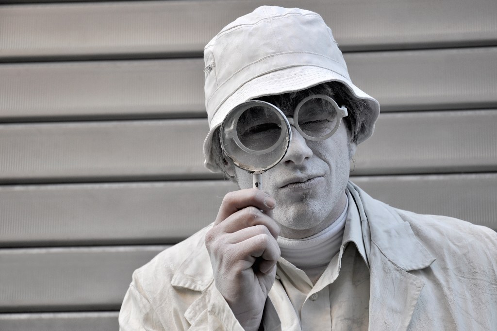 Living statue street performer posing in the center of Reggio Emilia with a magnifying class.
