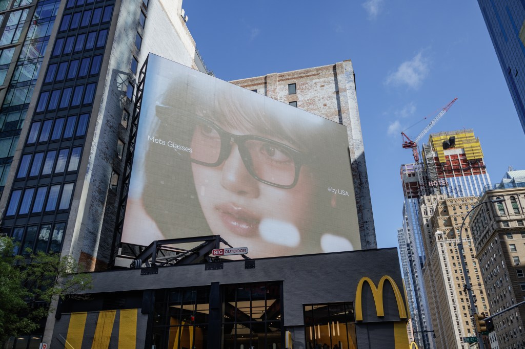 An advertisement for Meta Glasses is displayed on the side of a building at Eighth Avenue and West 42nd Street in Midtown Manhattan as a construction crane rises over a building under construction in the background.